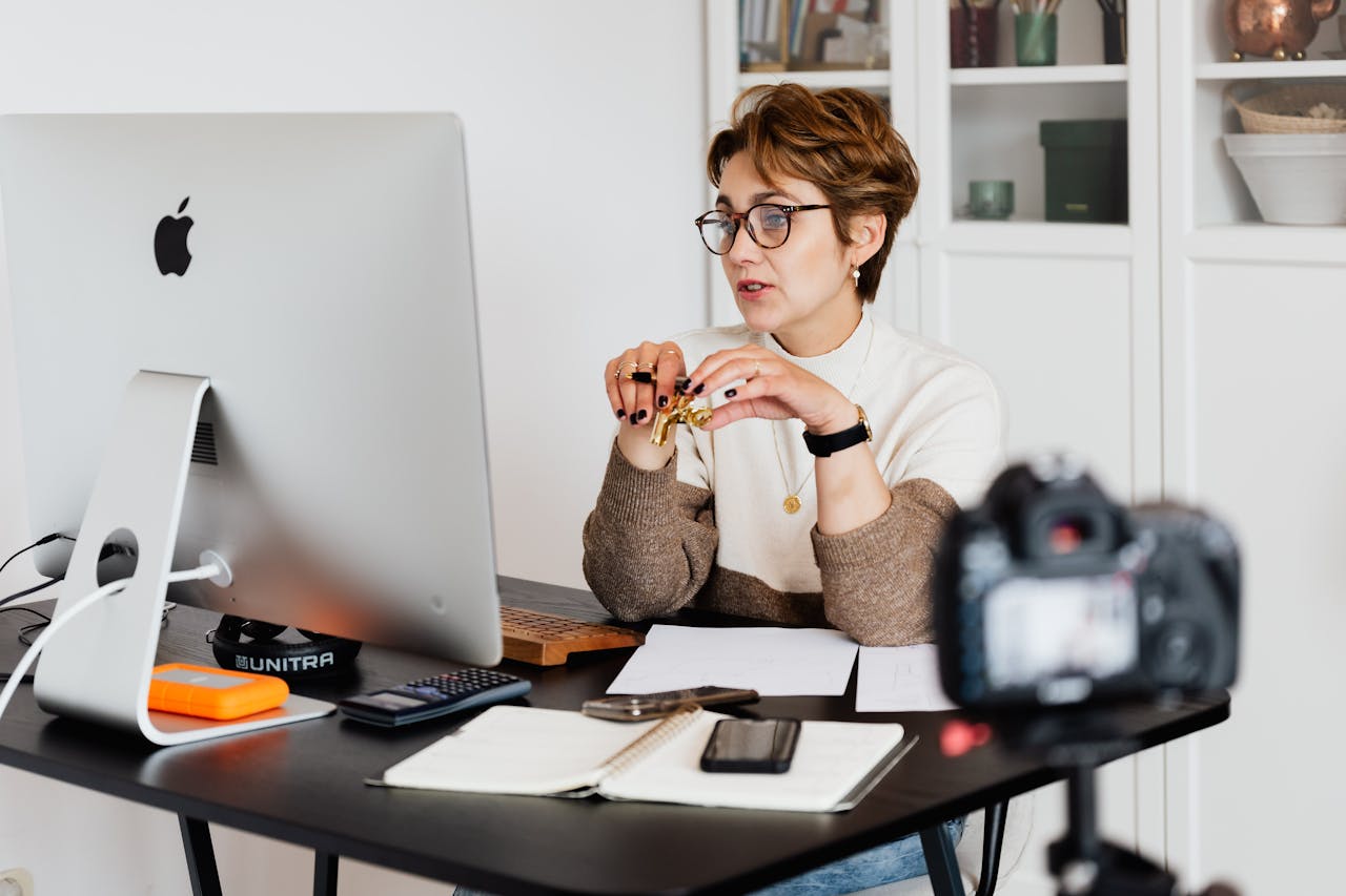 service-01 A professional woman engaged in a virtual meeting setup at her home desk, using a computer and camera.